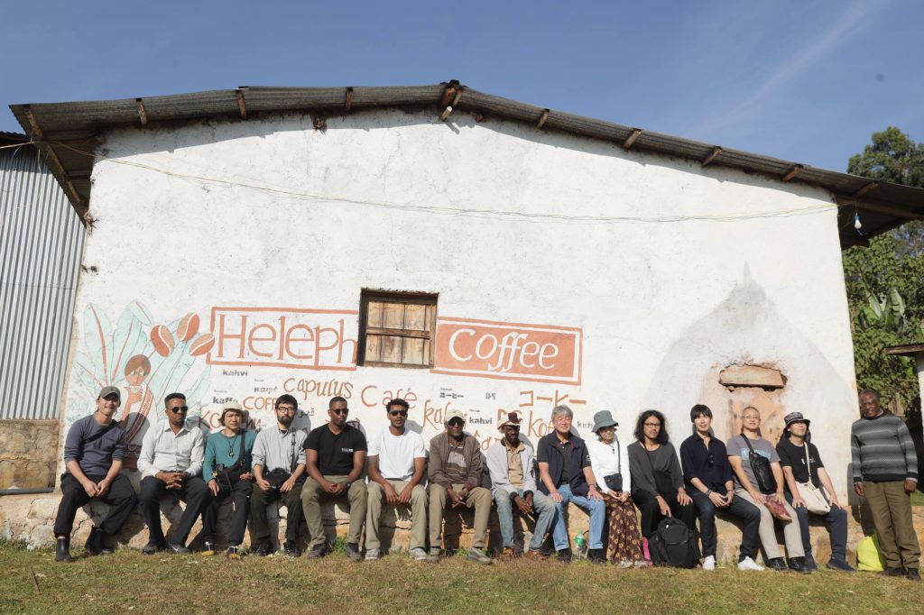 Coffee tour guests and the Heleph team seated in front of the painted Heleph Coffee wall